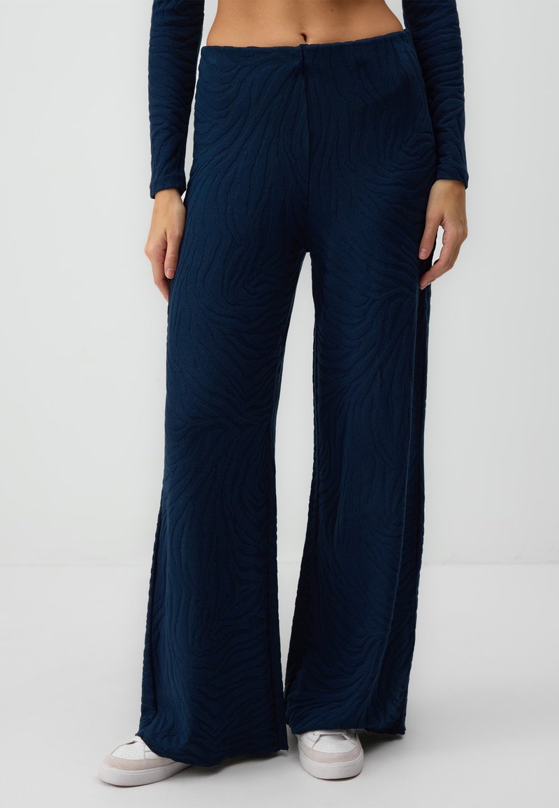 Navyblauwe flared broek van textuurstof met een zebra-streep patroon; hoge taille; gedragen met witte sneakers.