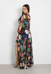 Rochie maxi florală dintr-un material negru transparent, cu culori vibrante, mâneci lungi și o deschidere. Designul include flori mari și frunze.