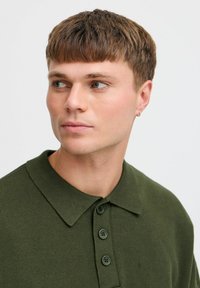 Grønn strikket polo skjorte med krage, med tre knapper foran og teksturert stoff. Skjorten har en klassisk passform og ensfarget design.