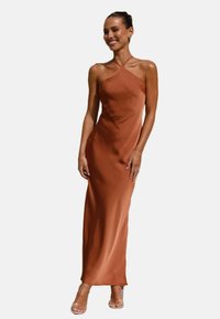 Maxikleid aus rostfarbenem Satin mit einem eleganten, figurbetonten Design, Spaghetti-Trägern und einer glatten, glänzenden Oberfläche. Durchsichtige Sandalen sind sichtbar.