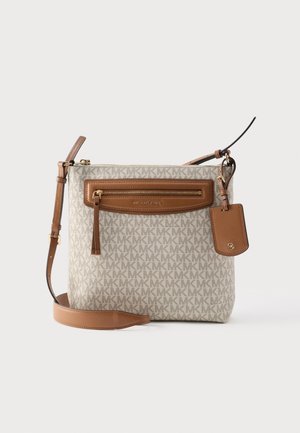 Beige crossbody bag with brown leather trim, front zipper pocket, adjustable strap, and a hanging tag with gold logo detailing.