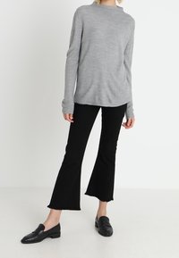 Grau, langärmliger Ripp-Strickpullover kombiniert mit schwarzen, ausgestellten Hosen mit rohen Säumen. Schwarze Loafers runden das Outfit ab.