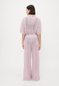 Conjunto de loungewear de punto en rosa claro, que incluye una blusa holgada de manga corta y pantalones de pierna ancha, ambos con un patrón texturizado y abierto.