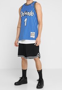 Maillot de basketball bleu avec des rayures verticales, des finitions noires et "Orlando" en lettres blanches. Accompagné de shorts et de chaussettes noires, et de baskets noires.