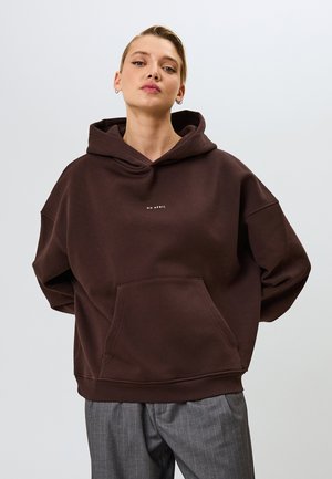 Brown hooded sweatshirt with a front pocket and white text "OH APRIL"; features loose fit and ribbed cuffs, paired with gray pinstriped pants.