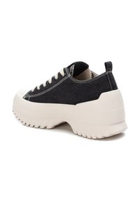 Zapatillas de lona negras con un upper texturizado, suela de goma off-white y costuras en contraste. Cuenta con una lengüeta en el talón.