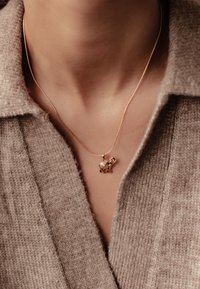 Collar con colgante de elefante de oro sobre una cadena delgada, con un diseño texturizado y pequeños acentos de gema, que se lleva sobre un suéter de punto beige.