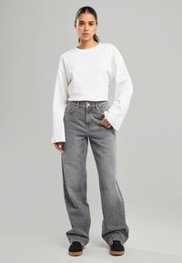 Haut à manches longues blanc avec un décolleté rond, assorti à un jean large taille haute gris clair. Baskets noires avec des semelles brunes.