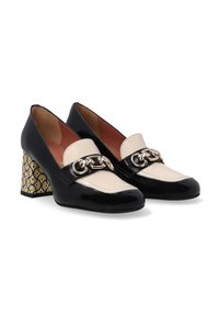 Zwarte en crèmekleurige lakleren schoenen met een lage blokhak, voorzien van een decoratieve gouden ketting en een patroon in geel en zwart op de hak.