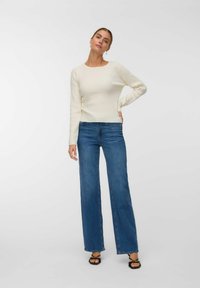 Off-white ribbad långärmad topp som är kombinerad med vida blå denimjeans, med hög midja och minimalistisk design.