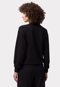 Felpa nera con collo rotondo, maniche lunghe e polsini a coste. Realizzata in materiale morbido, presenta un design posteriore rilassato.