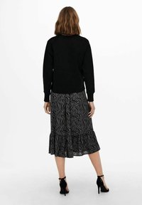 Suéter negro de manga larga combinado con una falda gris con volantes que presenta un patrón de rayas de cebra, completado con sandalias de tacón alto negras.