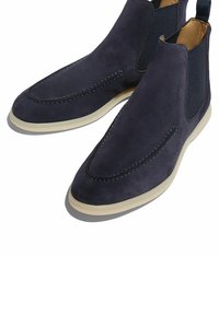 Botas Chelsea de ante en color navy con paneles laterales elásticos, una suela clara contrastante y costuras decorativas a lo largo de la puntera para un detalle adicional.