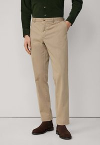 Beżowe chinosy o prostym kroju, wykonane z lekkiego materiału. Zawierają kieszenie boczne, zamek na guzik i są połączone z ciemnobrązowymi botkami za kostkę.