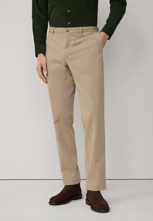 Chinos beige avec une coupe droite, confectionnés dans un tissu léger. Comprend des poches latérales, une fermeture à bouton, et assortis à des bottines marron foncé.