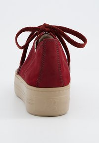 Sneaker rossa in suede con forma arrotondata, lacci coordinati e una robusta suola in gomma beige. Presenta dettagli di cucitura lungo le cuciture.