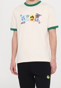 Cream t-shirt with green ribbed neckline featuring colorful cartoon bears and a yellow smiley face graphic, short sleeves, and relaxed fit.