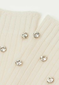 Tissu crème côtelé orné de rhinestones transparents, mettant en valeur un motif texturé et un subtil éclat grâce aux accents décoratifs.