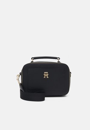 Sort rektangulær crossbody-taske med gyldent logo foran, top-hank og aftagelig bred rem, placeret mod hvid baggrund.