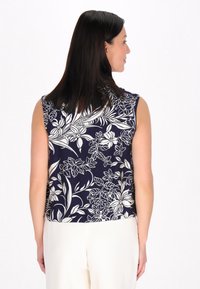 Top sin mangas en azul marino con diseño floral blanco, que presenta un escote redondeado y un corte holgado. Tejido suave con una textura fluida.