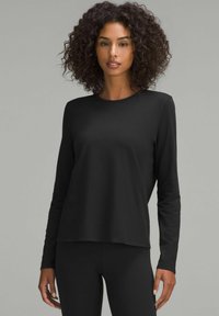 Maglietta nera a maniche lunghe in un tessuto morbido e liscio, con scollo rotondo e vestibilità rilassata. Indossata con leggings neri abbinati.