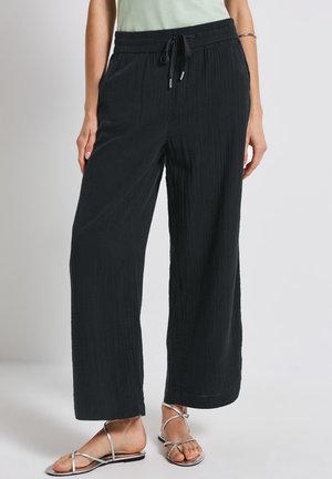 Zwarte, wijde broek van gestructureerde stof met een elastische tailleband en trekkoord. Gecombineerd met zilveren sandalen met banden.