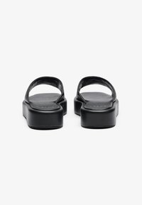 Black sandals with a flat, wide sole and two curved straps over the top. The material appears smooth and durable, featuring minimal detailing.
