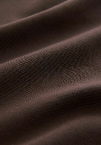 Tejido marrón texturizado con un suave brillo, que presenta un patrón de tejido sutil que crea pliegues y sombras suaves en toda la superficie.