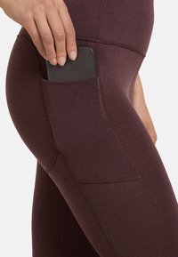 Bordeaux leggings van rekbaar materiaal met een zijzak voor een smartphone. Getextureerde afwerking met subtiele stikdetails.