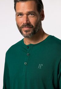 Polo shirt verde a maniche lunghe realizzato in cotone, con scollo a girocollo, tre bottoni e un logo discreto sul petto. Tessuto strutturato.