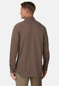 Hnědá košile s dlouhými rukávy vyrobená z měkké tkaniny, s rovnými okraji, klasickým límcem a zapínáním na knoflíky. Podrobné šití na ramenou.