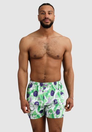 Badehorts aus einem Stoff mit grün-weißer Musterung, das lila Abbildungen von Früchten, Pflanzen und Blumen zeigt. Elastischer Bund.