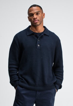Navy blue knitted pullover with a collar, featuring a button placket and ribbed texture. The design includes long sleeves and a relaxed fit.