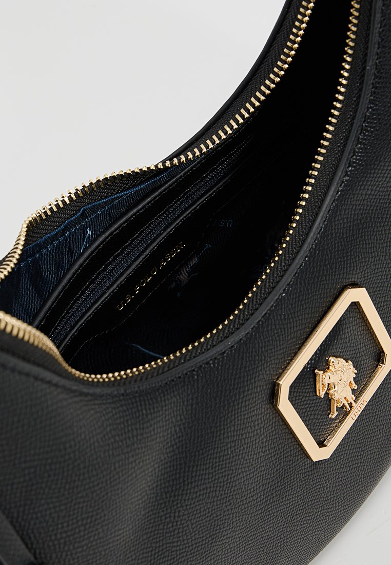 Sac à main en cuir noir avec une finition texturée, fermeture éclair dorée et logo embossé sur une plaque hexagonale. L'intérieur présente une doublure en tissu bleu et des compartiments.