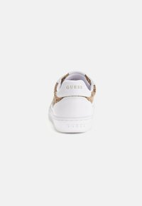 Sneaker bianco con dettagli in tan testurizzati. Presenta una punta arrotondata, suola piatta e il logo "GUESS" sul tallone e sul lato. Materiale complessivamente liscio.