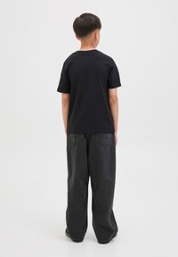 Crna pamučna majica s okruglim izrezom uparen s širokim tamnosivim trapericama. Odjeća je jednostavna, bez vidljivih uzoraka ili logotipa.