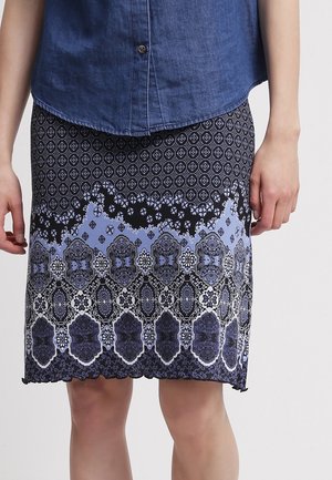 Jupe à motifs bleu et noir avec des motifs floraux et géométriques, en tissu léger et avec un ourlet festonné. Portée avec un haut en denim.