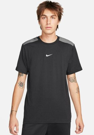 T-shirt de sport noir à manches courtes, encolure ronde, accents de couleur grise sur les épaules et petit logo Nike blanc sur la poitrine. Texture de tissu douce.