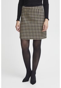 Spódnica w wzór houndstooth w kolorze jasnobrązowym i czarnym, o prostym kroju, z gładką fakturą, zestawiona z czarnymi rajstopami i szpilkami.