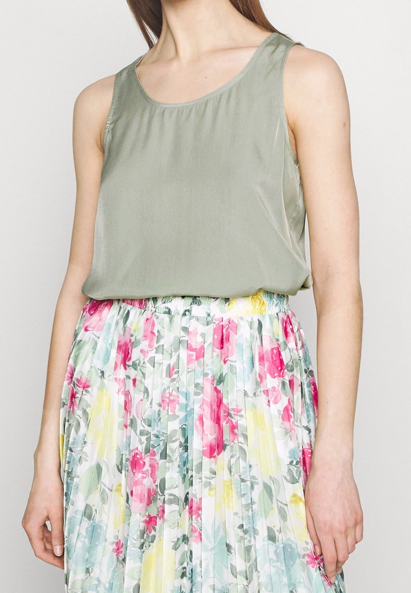 Top sin mangas de color verde oliva en tela suave, combinado con una falda plisada que presenta un estampado floral en tonos de rosa, amarillo y verde.