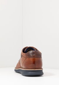 Chaussure en cuir marron, à coupe basse, finition lisse et texturée, semelle extérieure en caoutchouc, surpiqûres contrastantes, doublure intérieure bleue, design du talon arrondi.