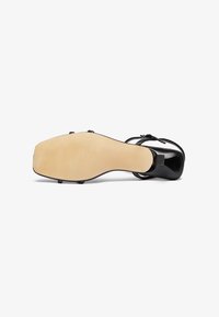Tacco in pelle nera con una finitura liscia e lucida. Punta squadrata e cinghietta sottile alla caviglia, con una suola in gomma beige.