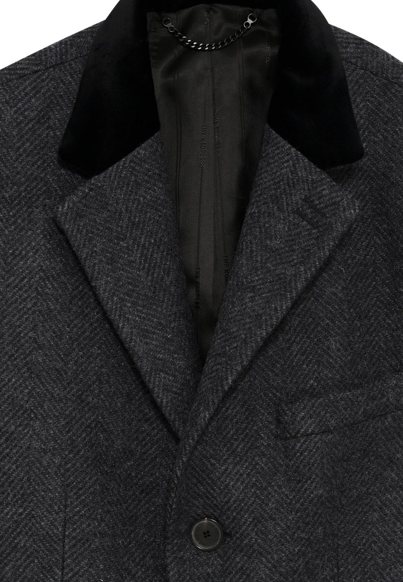 Gray herringbone wool blazer featuring a black velvet collar, single button closure, and a pocket on the left chest. Smooth interior lining.