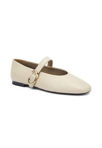 Zapato plano de cuero beige con punta redonda, que cuenta con una tira ancha con un detalle de hebilla dorada y un tacón bajo de goma negra.