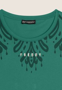 T-shirt verde in cotone con scollo rotondo, grafica frontale con motivo astratto verde scuro e logo metallico argento.