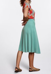 Zúžená sukně v mátové zelené barvě vyrobená z měkkého materiálu, s předními kapsami. Nošena s barevným, vzorovaným tričkem s krátkým rukávem a botami s leopardím potiskem.