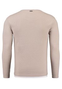 Beige Pullover mit langen Ärmeln, gerippter Textur und Rundhalsausschnitt, über einem weißen Unterhemd am unteren Saum getragen. Keine sichtbaren Logos.