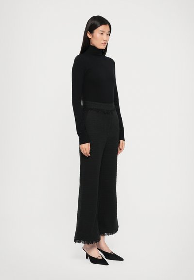 Black turtleneck sweater, paired with black textured wide-leg pants featuring fringed hem, and black pointed-toe high-heel shoes.