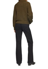 Olijfgroen gebreid sweater met een hoge kraag, gecombineerd met zwarte flared jeans en zwarte enkellaarsjes, gezien van achteren.