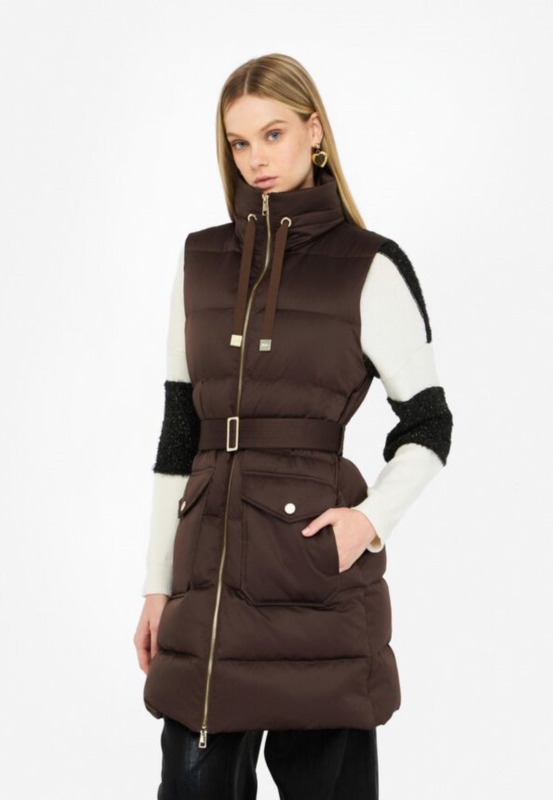 Gilet marrone imbottito con colletto alto, chiusura con zip, vita con cintura e tasche frontali. Presenta maniche texturizzate nere a contrasto.